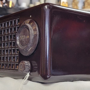 May include: A dark brown vintage Traveler radio with a grid-like speaker and a large tuning knob. The radio has a glossy finish and a rectangular shape.