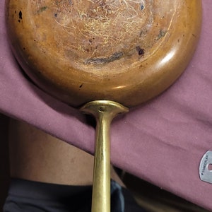 Puede incluir: Sartén de cobre vintage con mango de latón. La sartén tiene un aspecto desgastado y envejecido con una pátina marrón oscura. El mango está unido a la sartén con un anillo de metal.