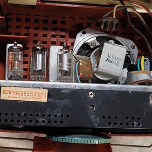 May include: Inside view of a vintage radio with three vacuum tubes, a speaker, and wiring. The radio has a black metal chassis with a label that reads "267B-19686583 Serial No. L.P.P. 115 Volts, A.C.-D.C., 20 Watts".