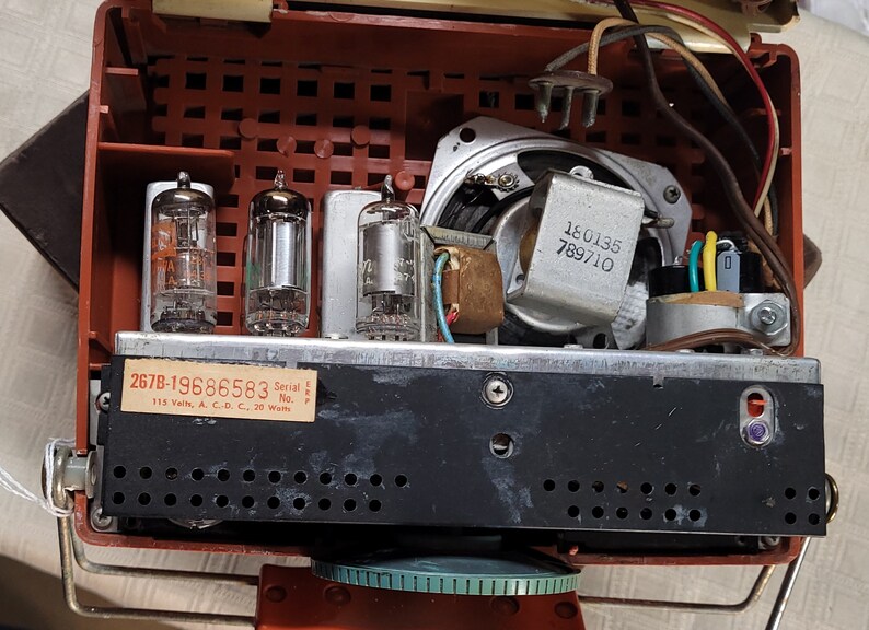 May include: Inside view of a vintage radio with three vacuum tubes, a speaker, and wiring. The radio has a black metal chassis with a label that reads "267B-19686583 Serial No. L.P.P. 115 Volts, A.C.-D.C., 20 Watts".