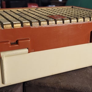 May include: A vintage, brown and white, rectangular radio with a gold-colored speaker grill. The radio has a hinged lid and a latch on the side.