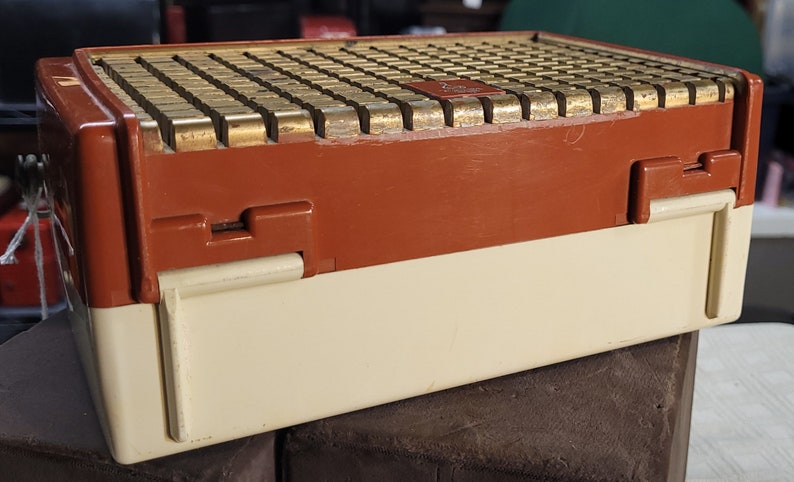 May include: A vintage, brown and white, rectangular radio with a gold-colored speaker grill. The radio has a hinged lid and a latch on the side.