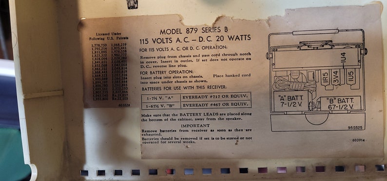 May include: Close-up of a vintage radio's back panel with instructions for using 115 volts AC/DC or battery power. The panel is beige with black text and a diagram showing battery placement. The text includes model number 879 Series B, 20 watts, and battery types Eveready #717 and #467.