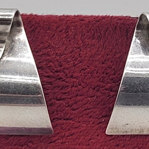 May include: A pair of silver earrings with a triangular shape. The earrings have a V-shaped cut-out at the top.