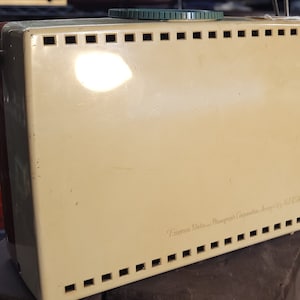 May include: A vintage cream-colored Emerson Radio and Phonograph Corporation, Jersey City, N.J. USA radio with a green knob and a metal grill.