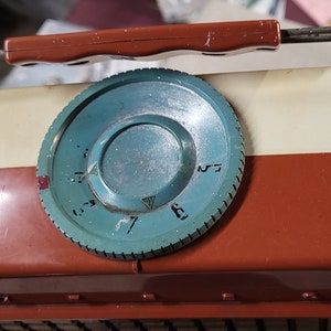 May include: A vintage, portable, brown and white radio with a teal knob. The knob has numbers 3 through 7 on it. The radio has a metal handle and a tag that reads "Tuning 1/2 - 77/4" and "6.4L.T.  Made in Japan".