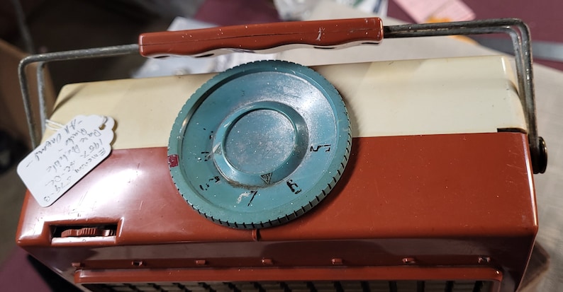 May include: A vintage, portable, brown and white radio with a teal knob. The knob has numbers 3 through 7 on it. The radio has a metal handle and a tag that reads "Tuning 1/2 - 77/4" and "6.4L.T.  Made in Japan".