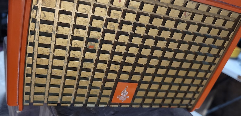 May include: A vintage orange and gold radio with a grid pattern on the front. The radio has a small orange label with the text "LOMAX" in white.