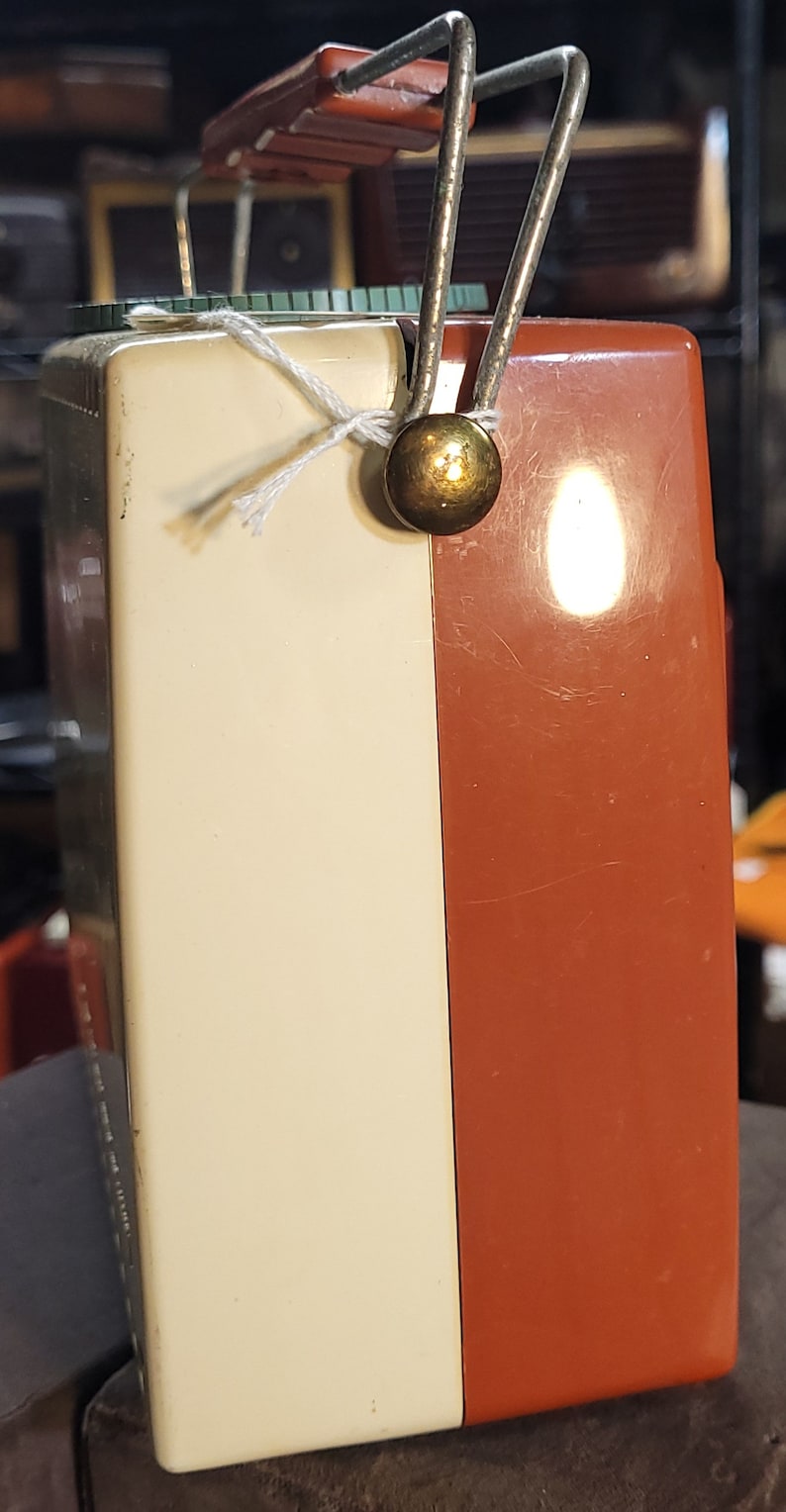 May include: A vintage portable radio with a white and orange plastic case. The radio has a metal carrying handle and a gold knob.