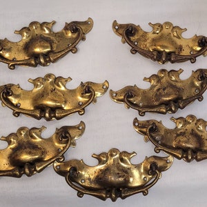 May include: Set of six antique brass drawer pulls with a bird design. Each pull has a decorative, ornate shape with a curved handle.