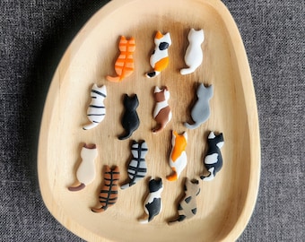 May include: A wooden plate with 15 small ceramic cat figurines in various colors and patterns. The cats are all sitting in a row, facing the same direction.