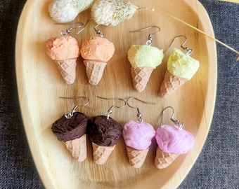 May include: Six pairs of ice cream cone earrings. The earrings are made of polymer clay and feature different ice cream flavors, including orange, yellow, chocolate, and pink.
