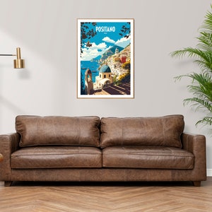 May include: A framed poster with a colorful illustration of Positano, Italy. The poster features a blue sky, white buildings, and a blue domed church. The text "Positano" is printed in white on a blue background at the top of the poster.