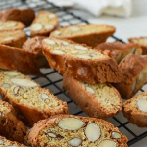 May include: A close-up of a plate of biscotti cookies. The cookies are golden brown and have a crispy texture. They are topped with almonds.