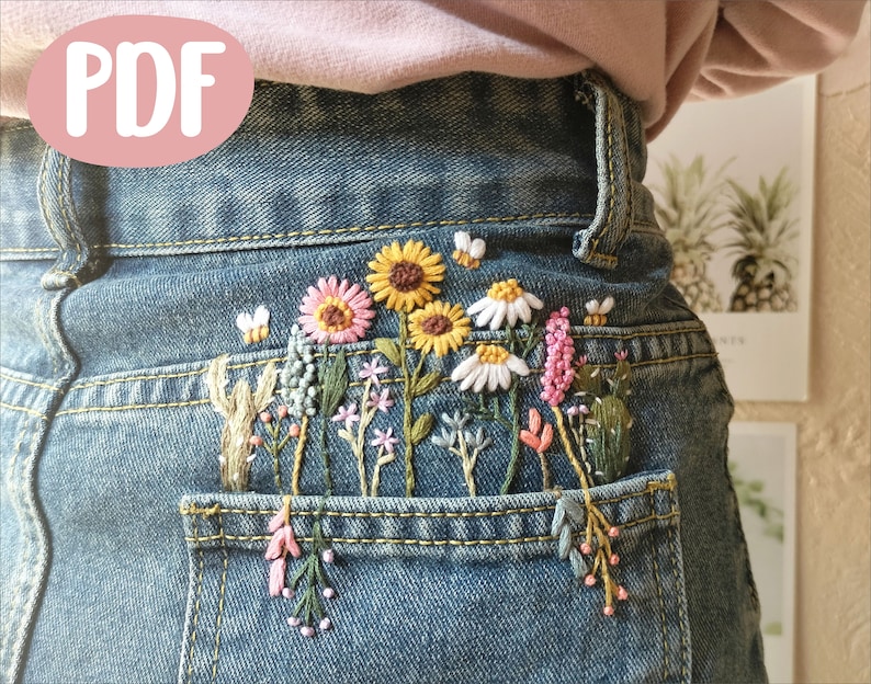 Pu&ograve; includere: Un paio di jeans blu denim con una tasca posteriore ricamata con un motivo floreale. Il ricamo comprende girasoli, margherite e altri fiori selvatici in tonalit&agrave; di giallo, rosa, bianco e verde.