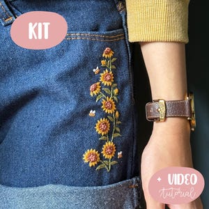 Puede incluir: Primer plano de unos shorts vaqueros con bordados de girasoles y abejas. El bordado utiliza hilo amarillo, naranja y verde. Los shorts tienen un dobladillo enrollado y un bolsillo. El texto en la imagen dice "KIT" y "+ VIDEO Tutorial".