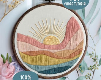Può includere: Un telaio da ricamo contenente un pannello in tessuto con un design paesaggistico cucito raffigurante un sole giallo con raggi radianti sopra colline stratificate nei toni del rosa, pesca, giallo senape e verde acqua. Testo PDF + VIDEO TUTORIAL.