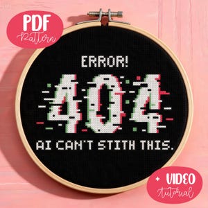 Pode incluir: Um bastidor de bordado circular de madeira contendo tecido preto com um design em ponto cruz. O design apresenta o texto branco ERROR! acima dos grandes números brancos 404 com um efeito glitch, seguido pelo texto AI CAN'T STITH THIS.