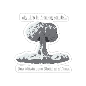 May include: A sticker featuring a stylized mushroom cloud graphic in shades of gray. Above the cloud, text reads "My Life is Manageable...". Below the cloud, the text continues "One Mushroom Cloud at a Time."