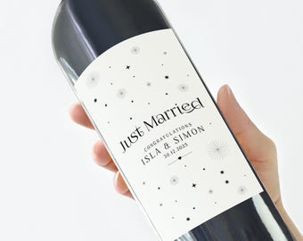 May include: A dark wine bottle with a white label that reads "Just Married" with the names Isla & Simon and the date 30.12.2025. The bottle has a dark green top and is held at an angle.