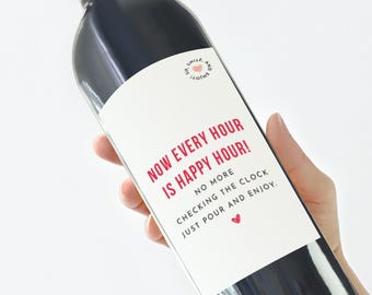 Puede incluir: Una etiqueta de botella de vino blanca con el texto "NOW EVERY HOUR IS HAPPY HOUR! NO MORE CHECKING THE CLOCK JUST POUR AND ENJOY." en rojo y negro.