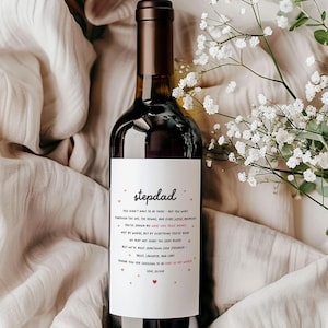 May include: A bottle of red wine with a white label that says "stepdad". The label has a message about being a stepdad and includes gold stars and a pink heart.