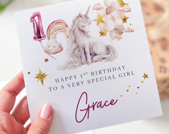 May include: A birthday card with a unicorn illustration, a rainbow, and the number 1 in a pink balloon. The card reads "Happy 1st Birthday To A Very Special Girl" and includes the name "Grace" in a cursive font.