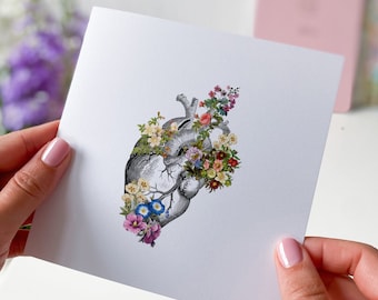 May include: A vintage anatomical heart illustration with colorful flowers blooming from it. The heart is in black and white, while the flowers are in various shades of pink, red, blue, yellow, and green.