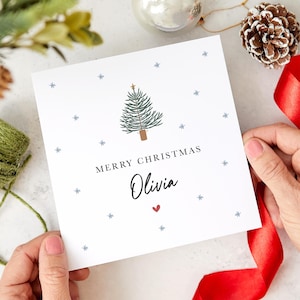 May include: A white Christmas card with a blue and green Christmas tree illustration, a gold star, and the text "Merry Christmas Olivia" with a red heart.