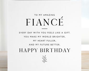 May include: A white birthday card with black text. The card says "TO MY AMAZING FIANCÉ" and includes the message "HAPPY BIRTHDAY". A small sprig of leaves is at the bottom.