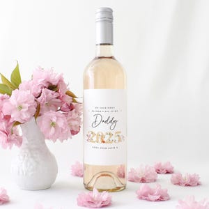 May include: A bottle of ros&eacute; wine with a white label that reads "On your first Father's Day as my Daddy 2025 Love from Alfie". The bottle is next to a white vase with pink flowers and scattered pink flowers.