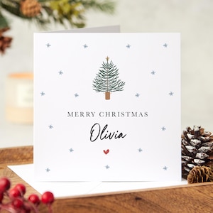 May include: A white Christmas card with a green Christmas tree illustration, snowflakes, and the text "Merry Christmas Olivia" with a red heart.