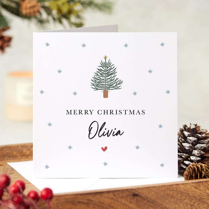 May include: A white Christmas card with a green Christmas tree illustration, snowflakes, and the text "Merry Christmas Olivia" with a red heart.