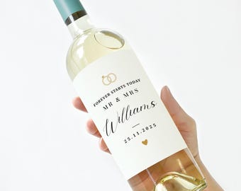 May include: A bottle of white wine with a teal cap and a white label. The label features gold rings, the words "FOREVER STARTS TODAY MR & MRS Williams" and the date 25.11.2025 with a gold heart.