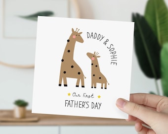 May include: A white card with two brown giraffes, one larger than the other. The text "Daddy & Sophie" is written in black cursive above the giraffes. Below the giraffes, the text "Our First Father's Day" is written in black.