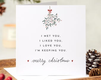May include: A white Christmas card with a red bow and green mistletoe illustration. The card reads "I met you, I liked you, I love you, I'm keeping you. Merry Christmas."