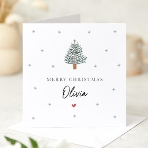 May include: A white Christmas card with a green Christmas tree illustration, a gold star on top, and the text "Merry Christmas Olivia" with a red heart.