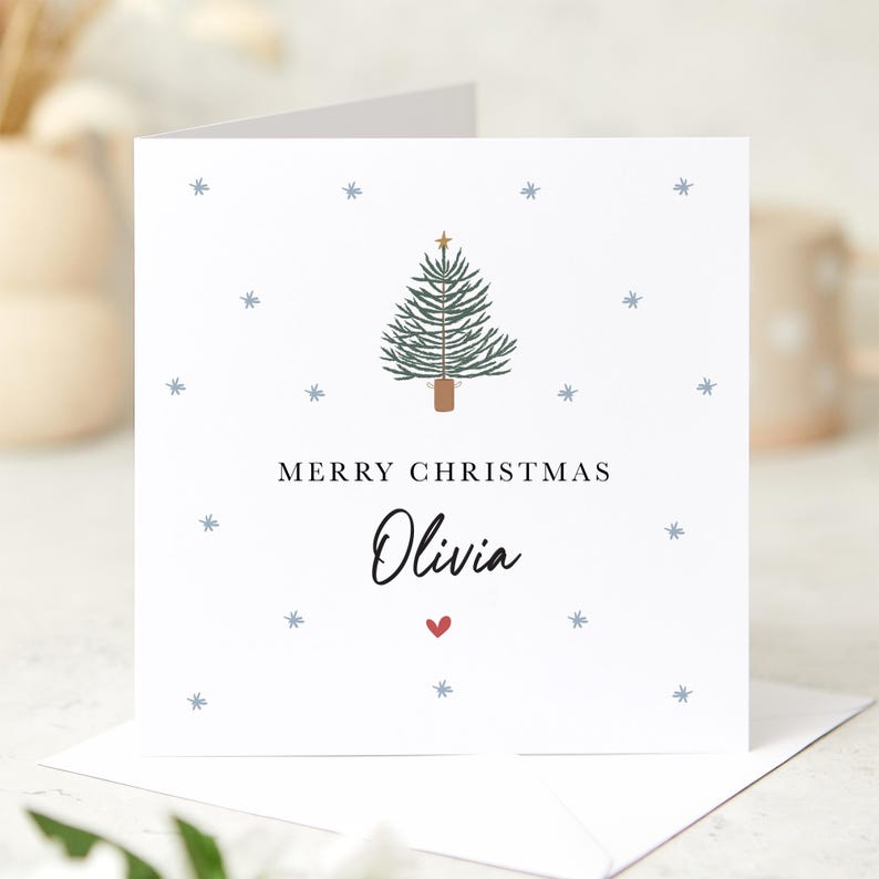 May include: A white Christmas card with a green Christmas tree illustration, a gold star on top, and the text "Merry Christmas Olivia" with a red heart.