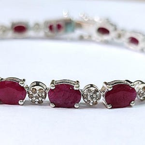 May include: A silver bracelet with oval-shaped red ruby gemstones and smaller clear gemstones. The bracelet is made of sterling silver and features a classic design.