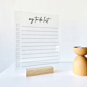 May include: A clear acrylic to-do list board with a black inscription that reads "my to-do list". The board has a wooden stand and is sitting on a white surface.