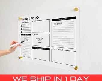 May include: A white dry-erase board with black lines and text. The board is divided into sections labeled "Things to Do", "Don't Forget", "This Week", "To Do List", "Events", "Reminder", "Not Important", and "Next Week". The board is mounted on a white wall with gold-colored push pins.