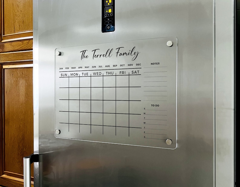 May include: A clear acrylic dry-erase calendar and to-do list with the text "The Terrell Family" at the top. The calendar has spaces for each month of the year and days of the week. There are also spaces for notes and a to-do list.