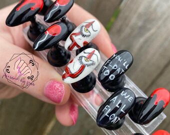 Puede incluir: Conjunto de uñas postizas con un diseño negro y rojo inspirado en la película "It". Las uñas presentan un globo rojo, una cara de payaso y el texto "You'll float too" y "We all float".