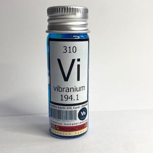 May include: A small, clear glass bottle with a silver lid. The bottle contains a blue liquid and has a white label with the text "310 Vi vibranium 194.1" and a barcode. The label also includes the text "ity: Earth-616, Earth-199999 Vb Creation: Extraterrestrial RADIOACTIVE Research Sample".