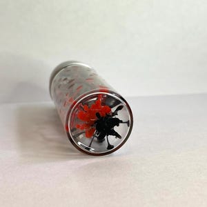 K&ouml;nnte beinhalten: Ein klares Glasrohr mit einem roten und schwarzen Wirbelmuster im Inneren. Das Rohr ist an beiden Enden versiegelt.