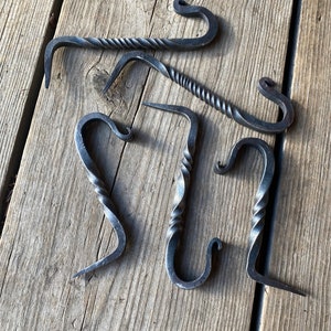 May include: Five twisted metal hooks with a rustic finish. The hooks are arranged in a semi-circle on a wooden surface.