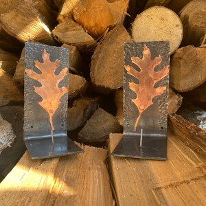 May include: Two black metal wall hooks with copper leaf designs. The hooks are mounted on a wooden surface.