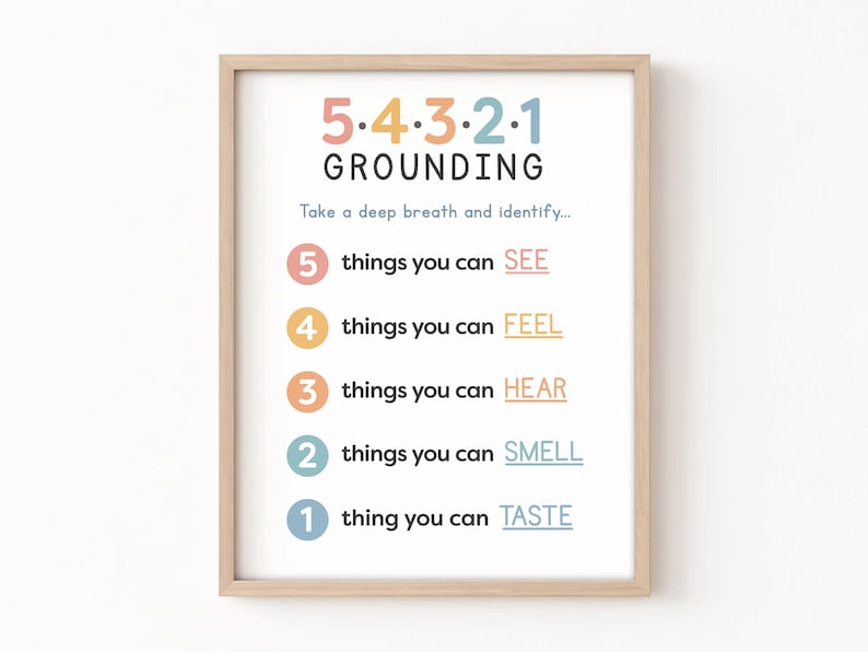 May include: A framed print with the text "5-4-3-2-1 GROUNDING." The print provides a mindfulness exercise, listing steps to identify things you can see, feel, hear, smell, and taste. The text is in various colors, with a light wood frame.