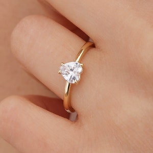 Può includere: Un anello d'oro con una pietra preziosa trasparente a forma di cuore.