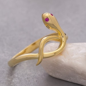 Può includere: Un anello a forma di serpente in oro con due pietre preziose rosa per gli occhi.
